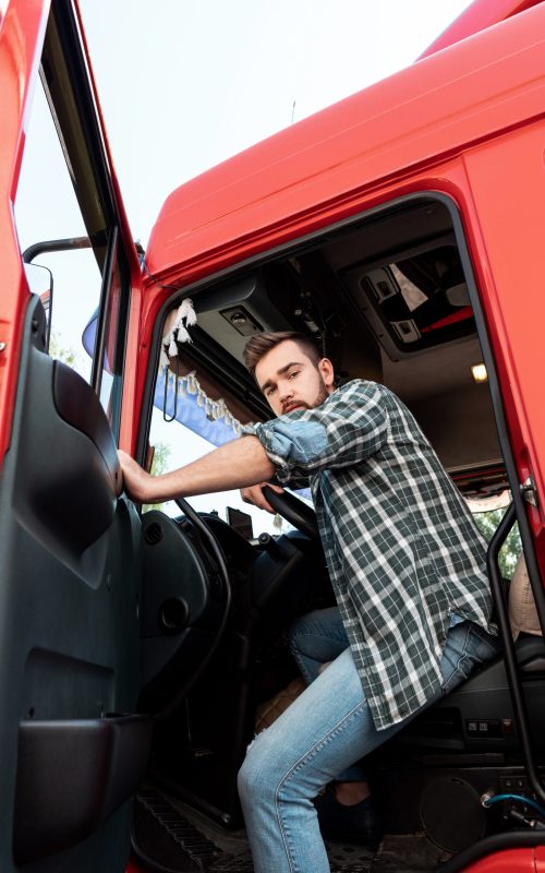Handsome bearded truck driver sitting inside his red cargo truck