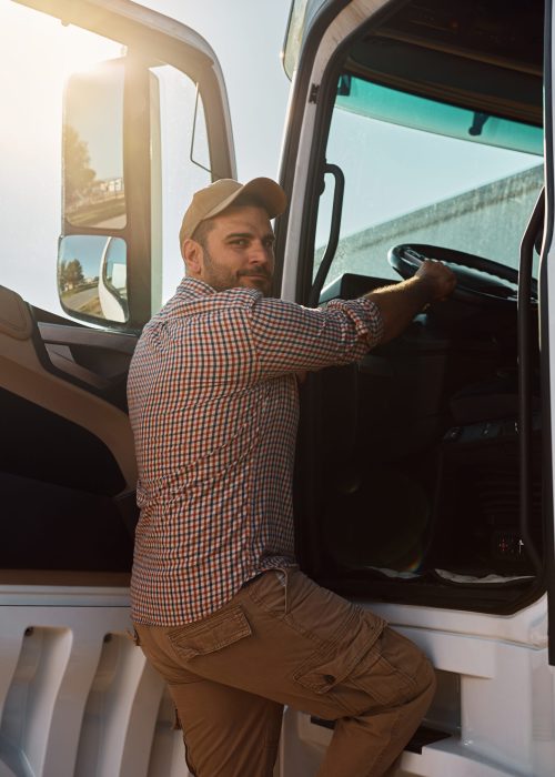 Young  truck driver getting into vehicle cabin and looking at camera.