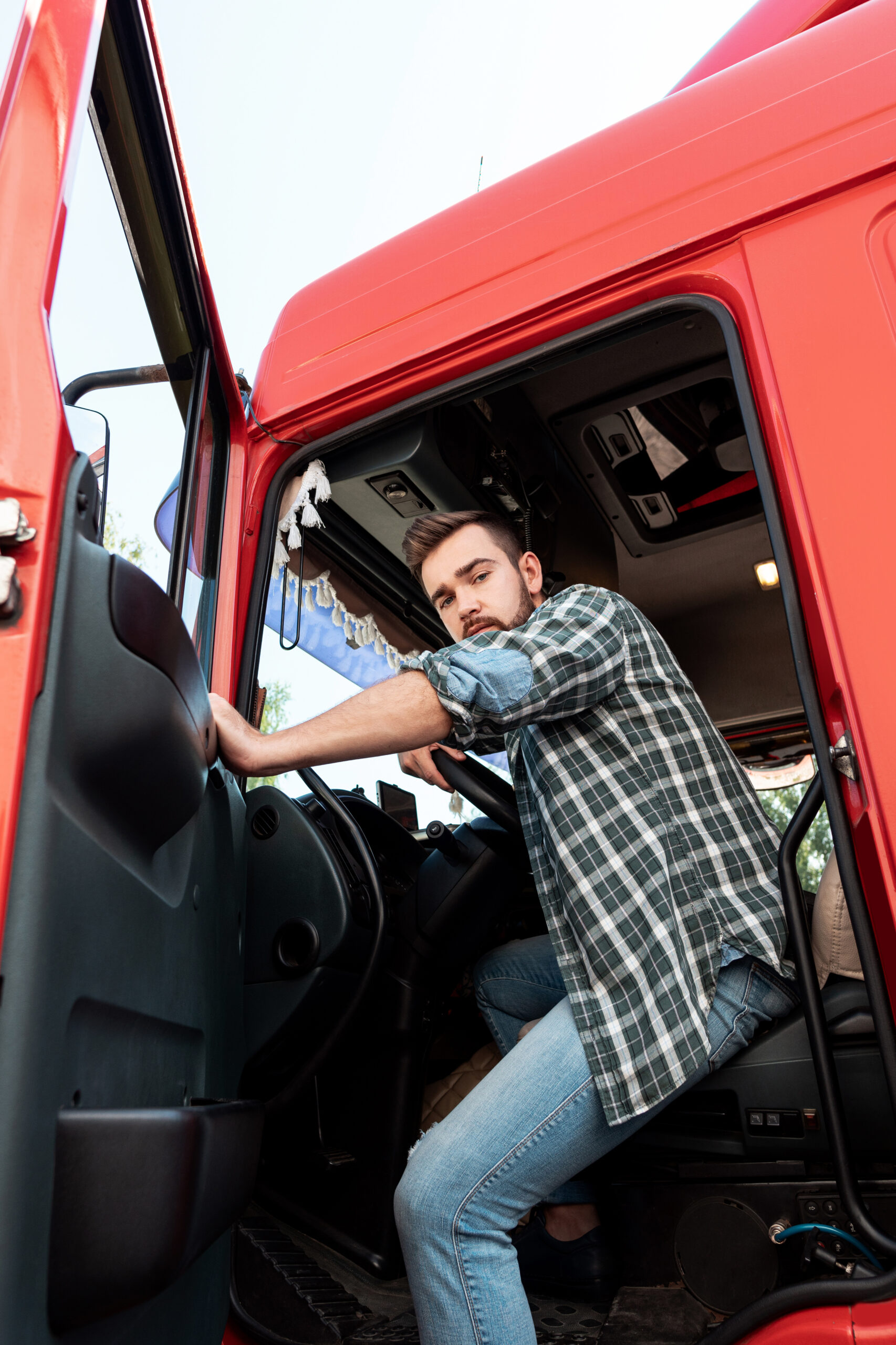 Handsome bearded truck driver sitting inside his red cargo truck